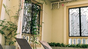 Un espace extérieur aménagé, abrité et doté de chaises en métal, ainsi qu’une pergola couverte de plantes grimpantes en fleurs.