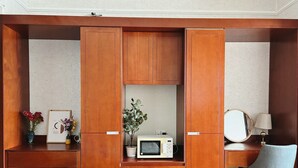 Une pièce de taille modeste, comprenant un bureau en bois, une chaise, un four à micro-ondes et un petit meuble avec un miroir et une lampe.