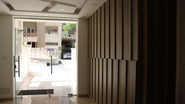 Un hall d’hôtel moderne avec une porte vitrée donnant sur l’extérieur, un sol carrelé et un mur revêtu de panneaux en bois.