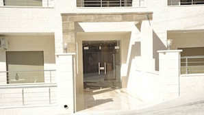 Une entrée d’immeuble avec une porte en verre, un portail en métal et un chemin en béton menant à la porte.