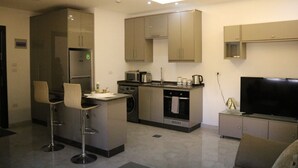 Een moderne keuken met een inbouwoven, magnetron en spoelbak. Er staan twee barkrukken en een grote flatscreen televisie.