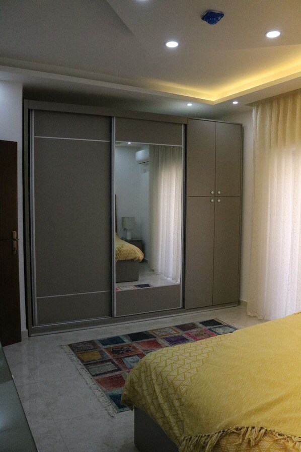 A bedroom with a bed, a wardrobe, a mirror, and a window with curtains. - Amazing one Bedroom Apartment in Amman,Elwebdah 8 (Amman)