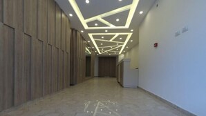 Een gang met houten paneelbekleding, een gepolijste marmeren vloer en een plafond met ingebouwde verlichting en geometrische patronen.