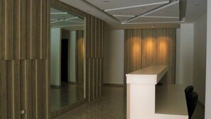 Un interno moderno con un lungo corridoio, pareti rivestite in legno, una reception bianca e una porta in vetro che dà su un'altra stanza.