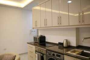 A compact kitchen with a microwave, kettle, and washing machine. - Amazing one Bedroom Apartment in Amman, Elwebdah 7 (Amman)