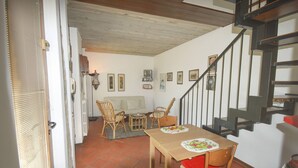 Ein Essbereich mit Holztisch und -stühlen, eine Treppe und ein Wohnzimmer im Hintergrund.