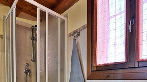 Un espace douche doté d’une porte en verre, d’un porte-serviettes avec une serviette, et d’une étagère contenant des serviettes pliées et des paniers.