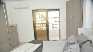 Un dormitorio con cama, armario, puerta corrediza de vidrio y vista a edificios.