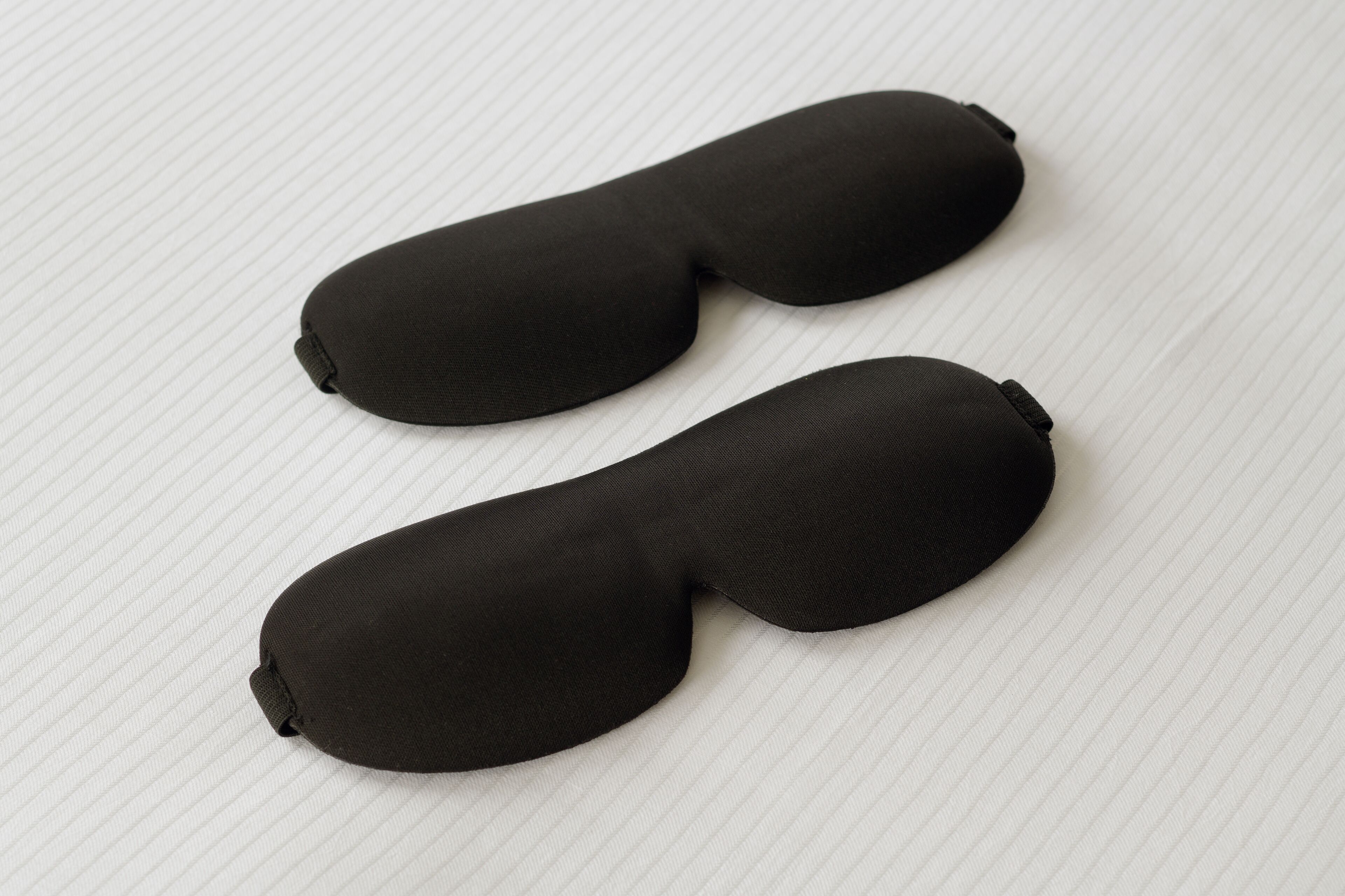 Dos objetos negros, con textura acanalada, con forma de almohada sobre una superficie blanca y texturizada.