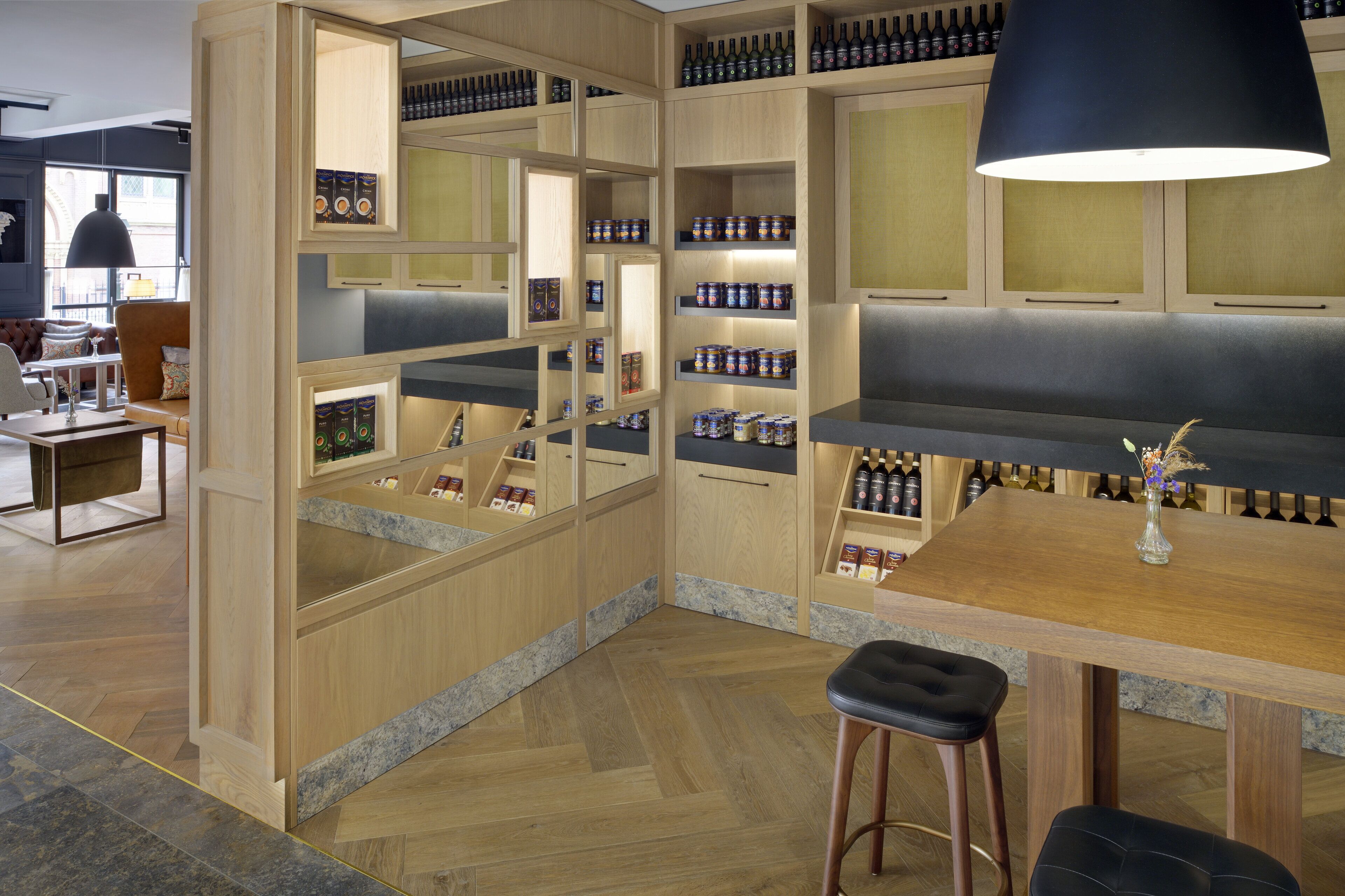 A modern bar area with wooden shelves displaying bottles and cans, a bar counter, and seating with stools.