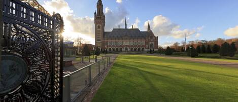 A large building with a prominent clock tower, surrounded by a well-maintained lawn and a decorative metal fence.
