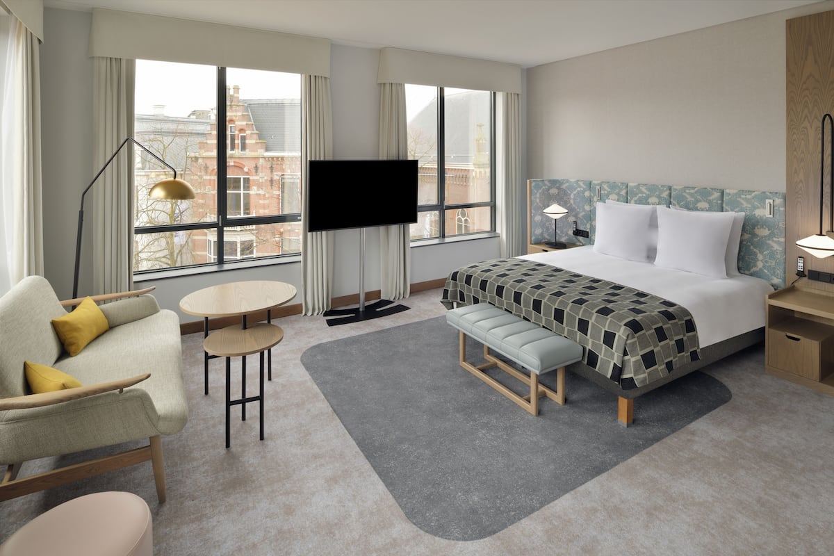 A modern hotel room with a large bed, a sofa, a small table, and a TV.