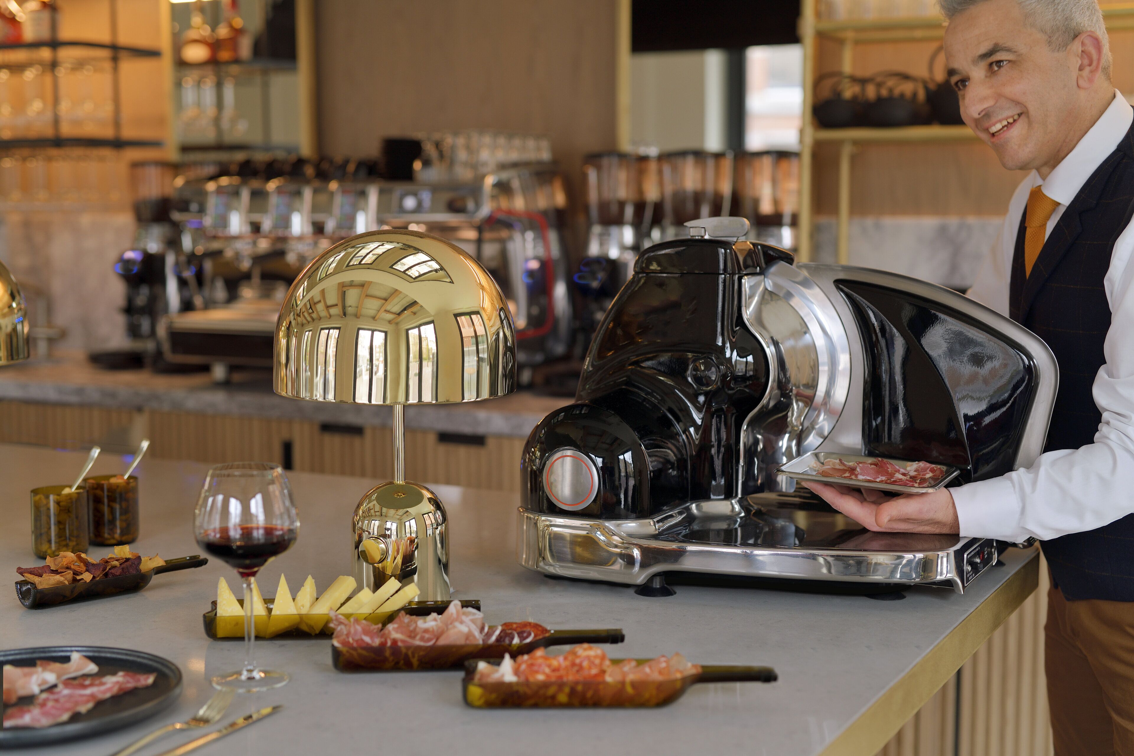 A bar area with a coffee machine, a wine glass, and various food items on the counter.