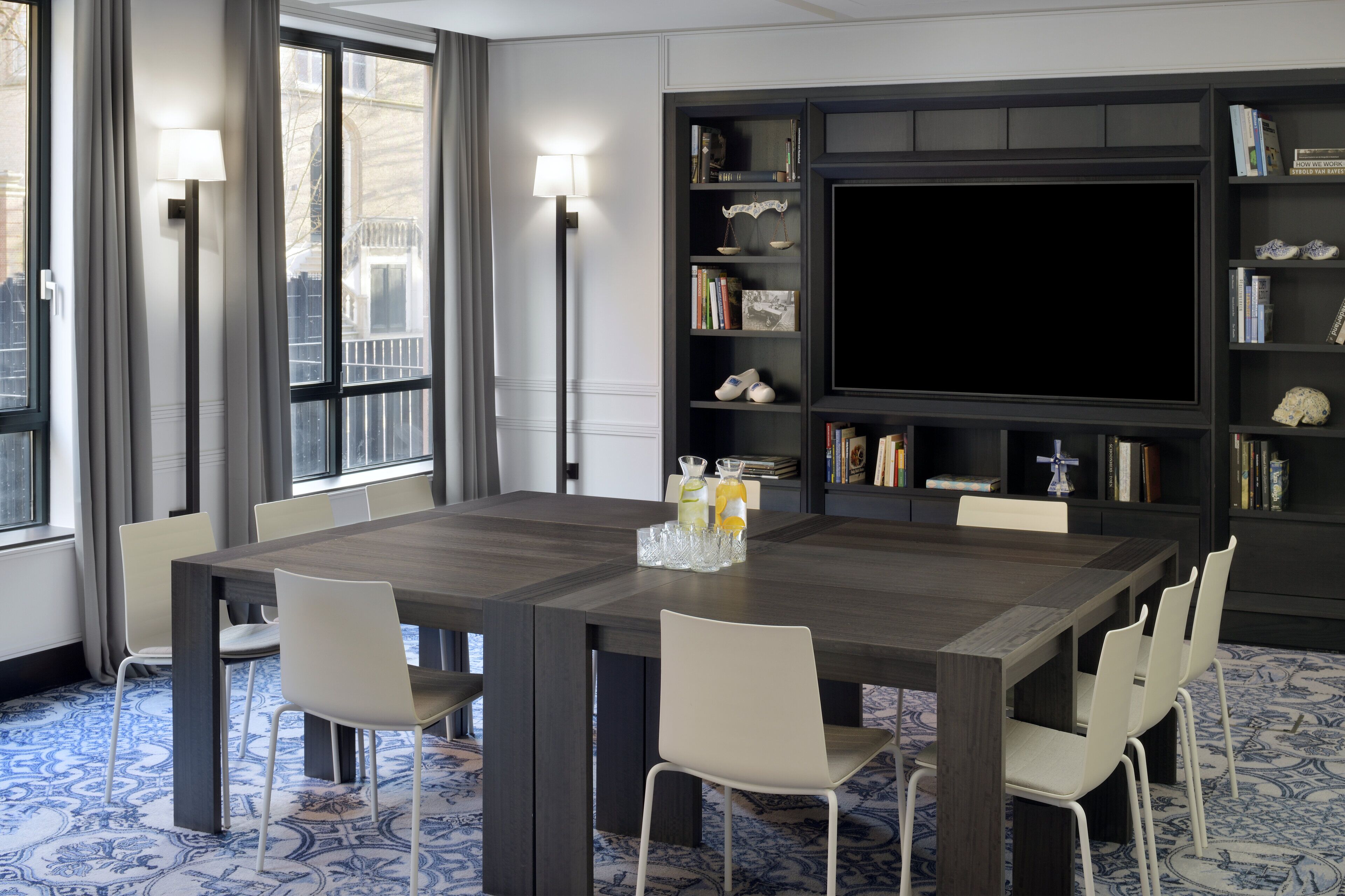 Uma área de jantar moderna com uma mesa grande, cadeiras brancas, uma estante de livros e uma televisão de tela plana.