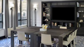 Uma área de jantar moderna com uma mesa grande, cadeiras brancas, uma estante de livros e uma televisão de tela plana.