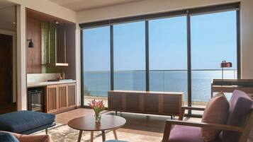 A modern living room with a large window overlooking the sea, a round wooden table, and comfortable seating.