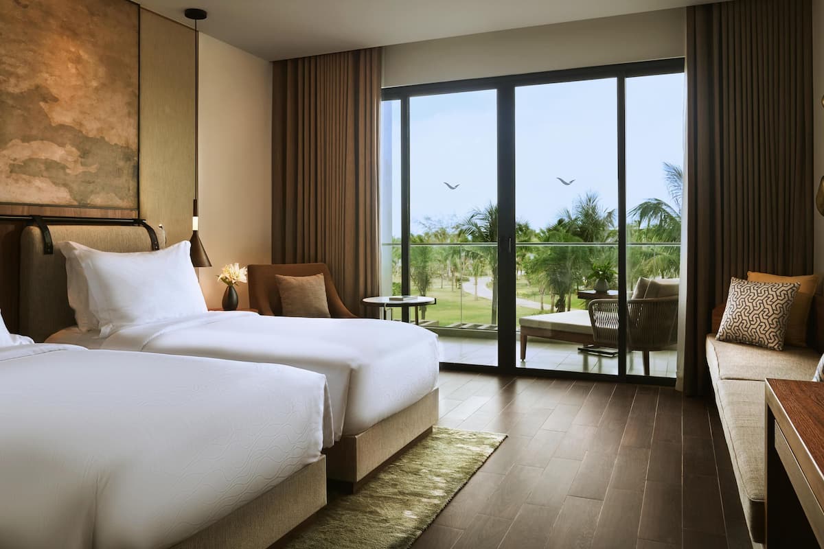 A hotel room with two beds, a balcony with a view of palm trees, and a seating area with a table and chairs.