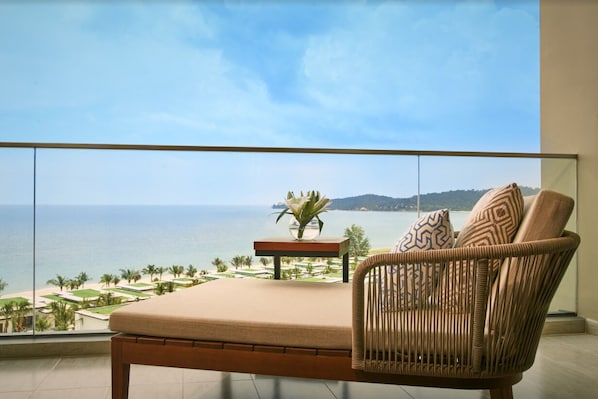 Ein Balkon mit Meerblick, ein Korbstuhl, ein kleiner Tisch mit einer Vase und ein Kissen.
