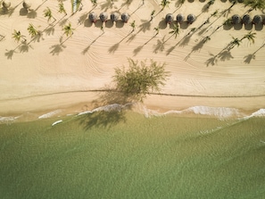 An aerial view of a beach with palm trees, a lone tree, and several spherical structures. - Mövenpick Resort Waverly Phu Quoc (Phu Quoc)