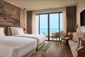 A hotel room with two beds, a balcony with a view, a seating area with a table, and a large artwork on the wall.