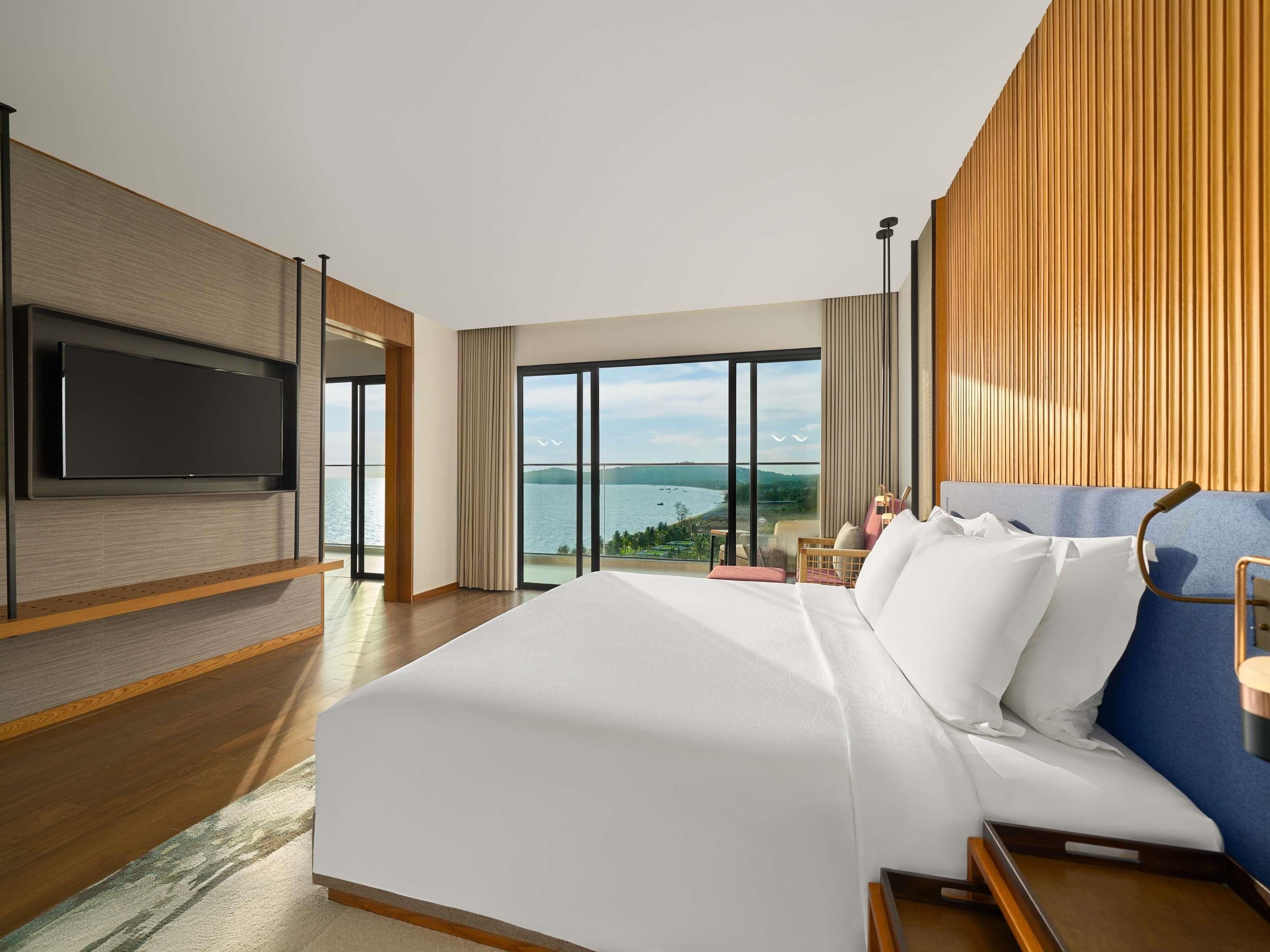 A hotel room with a large bed, a television mounted on the wall, and a view of the sea.