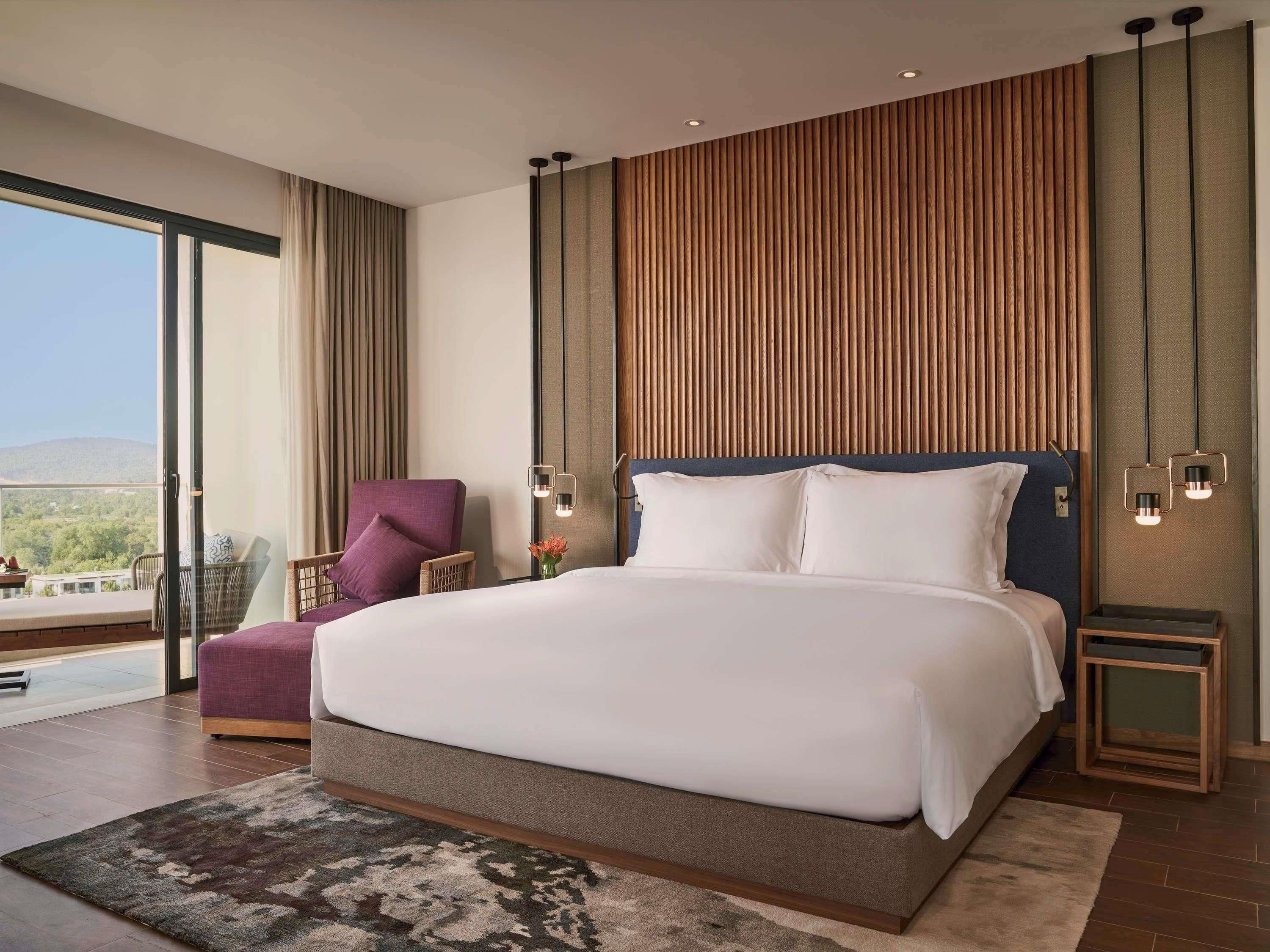 A modern hotel room with a large bed, a view of the outdoors, and a balcony.