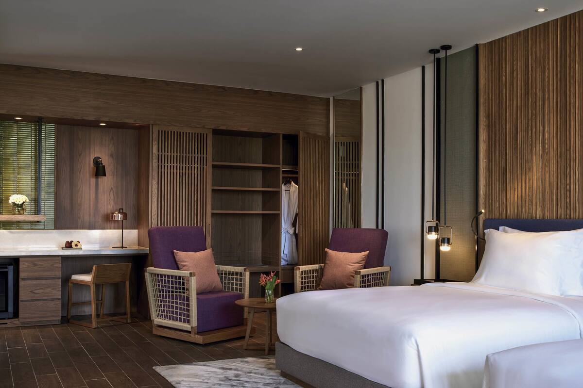 Ein modernes Hotelzimmer mit einem großen Bett, zwei Sesseln, einem Schreibtisch und einem Kleiderschrank.