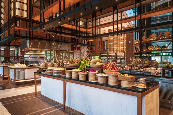A spacious hotel lobby with a central island featuring a variety of food items and decorative elements.