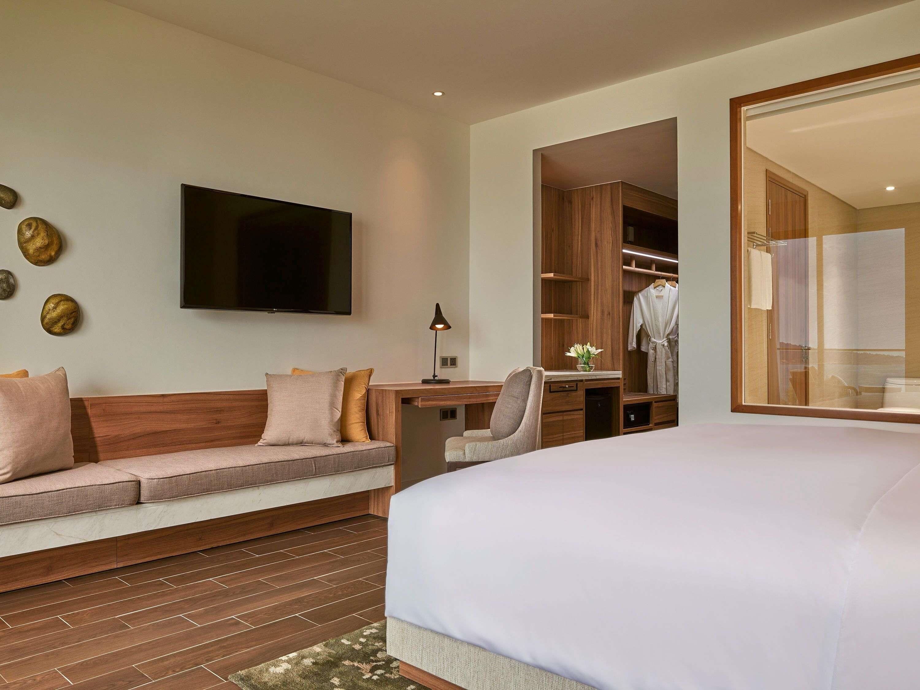 Una habitación de hotel moderna con una cama grande, un sofá, un escritorio, un televisor y un vestidor.