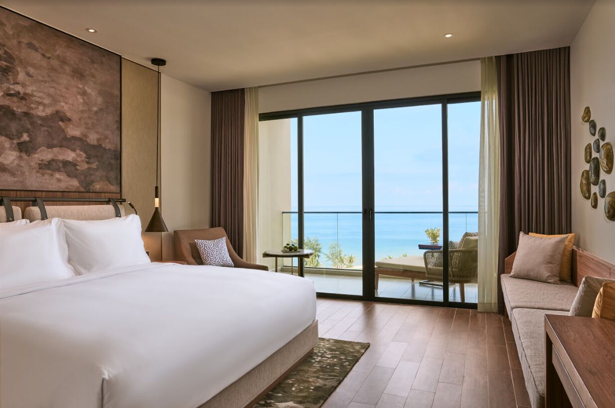 Une chambre d’hôtel dotée d’un grand lit, d’un balcon avec vue sur la mer et d’un coin salon avec une table et des chaises.