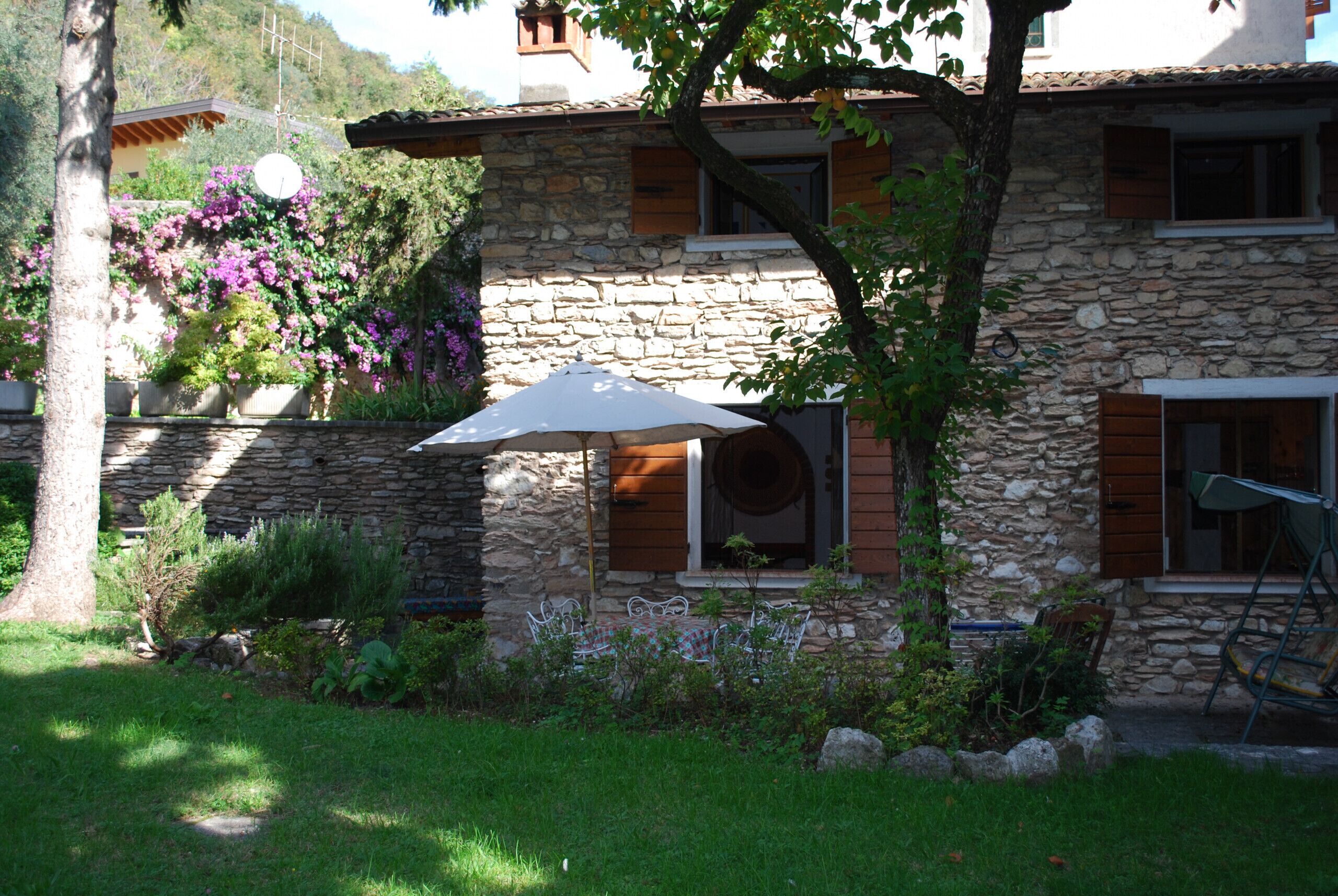 Un edificio de piedra con patio, mobiliario exterior y un árbol que da sombra.
