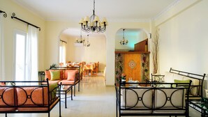 A spacious hotel lobby with a central seating area, a dining area, and a decorative wall with a fruit motif. - Karidis (Santorini)