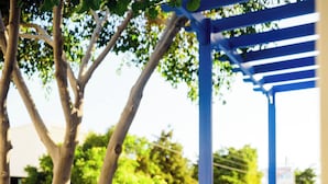 An outdoor cafe with blue and white furniture, a pergola, and trees in the background. - Karidis (Santorini)