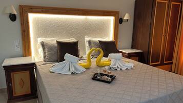 A neatly made bed with a patterned bedspread, two brown pillows, a decorative headboard, and a tray with a glass and a bottle.