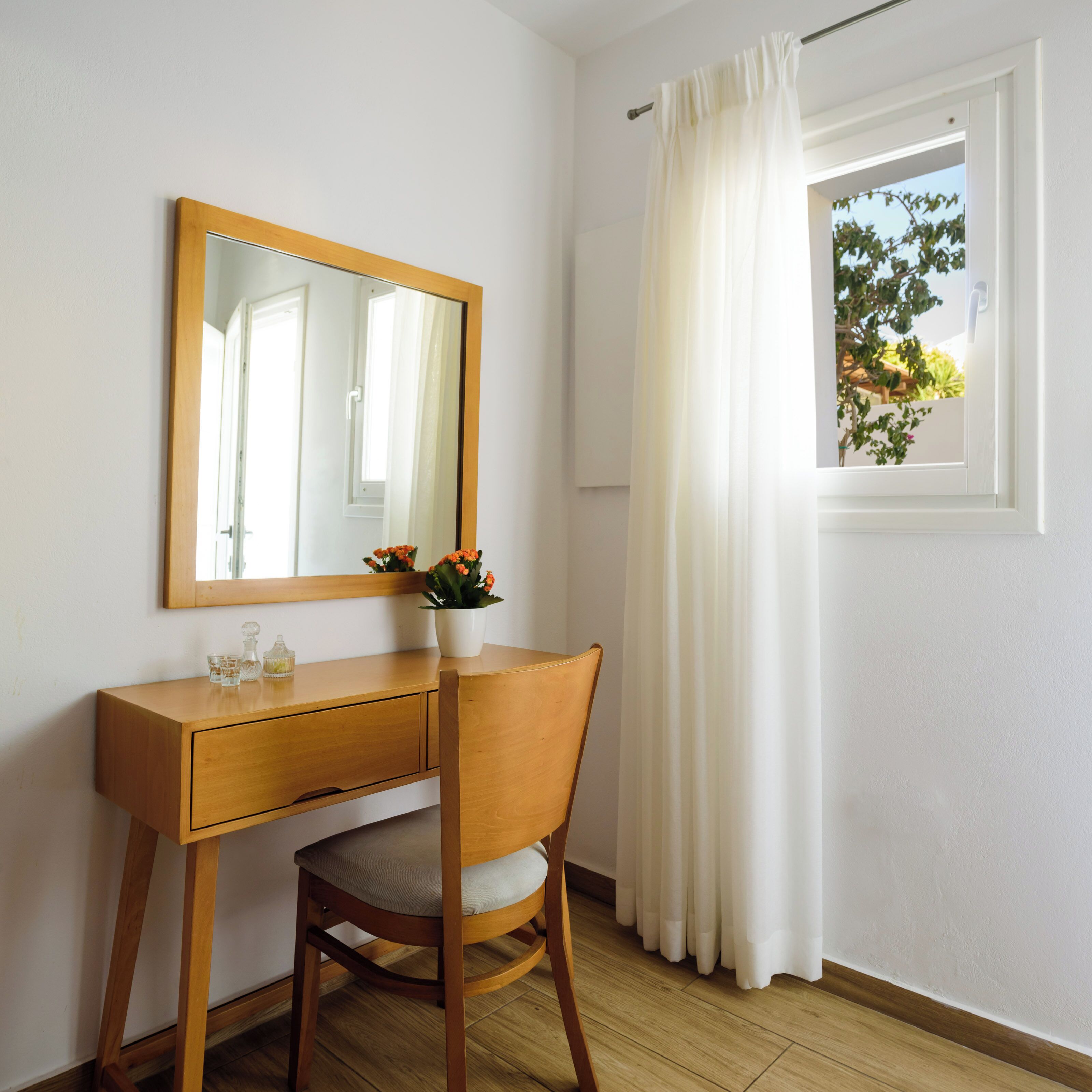 A wooden desk with a mirror, a chair, and a window with white curtains.