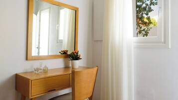 A wooden desk with a mirror, a chair, and a window with white curtains.