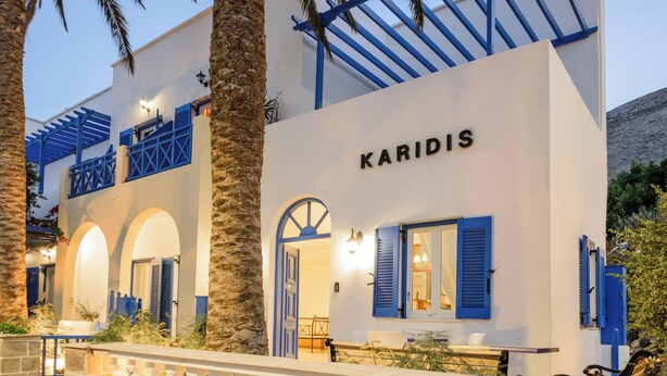 A building with the name "KARIDIS" on the facade, featuring a stone wall, blue shutters, and a balcony with white balustrades. - Karidis (Santorini)