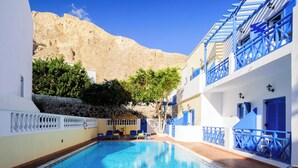 A swimming pool with blue tiles, a stone wall, and a mountain in the background. - Karidis (Santorini)