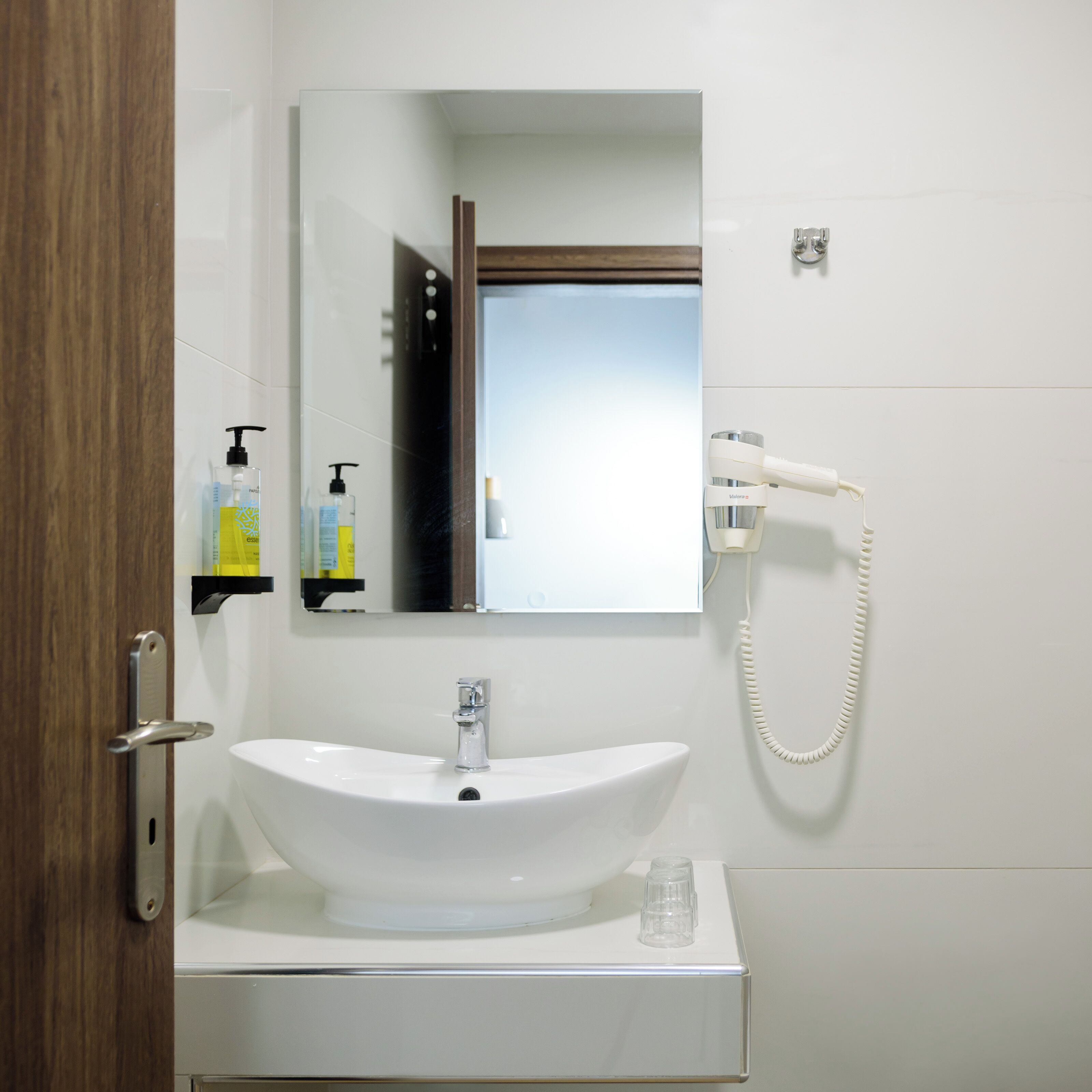 A bathroom with a white sink, a mirror, a handheld showerhead, and a bottle of shampoo.