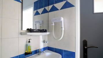 Un baño con lavamanos blanco, azulejos azules y blancos, un perchero, un secador de pelo y una botella de jabón para manos.