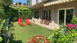 Une maison avec un patio, des chaises rouges et un jardin où poussent des fleurs rouges.