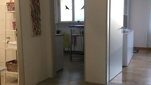 A hallway leading to a kitchen with a window, a door, and a tiled floor.