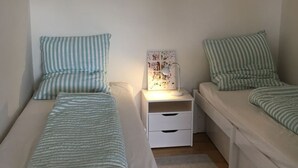 A bedroom with two single beds, each with striped bedding and pillows, a bedside table with a lamp, and a hanging light fixture.