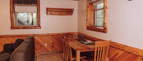 A cozy room with a wooden ceiling, a dining table with chairs, a sofa, and two windows with curtains.