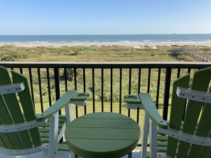 A balcony with two green Adirondack chairs and a small table, overlooking a beach with a distant ship and grassy dunes. - 3rd Floor Beachfront Condo with a Fantastic view of the Gulf —Sleeps 2.  (Galveston)