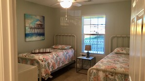 Une chambre avec deux lits, un ventilateur de plafond, une fenêtre avec des stores et un tableau au mur.