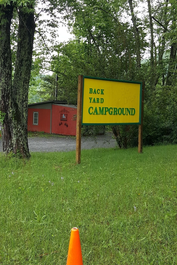 Une enseigne indiquant un « camping aménagé dans un jardin », avec un bâtiment rouge en arrière-plan.