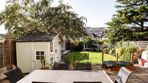 A patio with a table and chairs, a small shed, and a fenced yard with a lawn and trees. - Harrington House (Bristol)