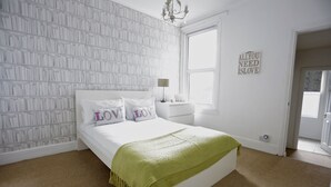 A bedroom with a white bed, green throw, and a wall with a 'You need is love' sign. - Harrington House (Bristol)