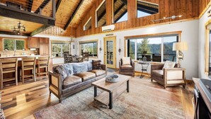 A spacious living area with a high ceiling, wooden beams, and large windows offering views of the outdoors.